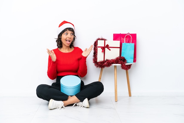 Jeune fille célébrant Noël assis sur le sol isolé sur fond blanc avec une expression faciale surprise