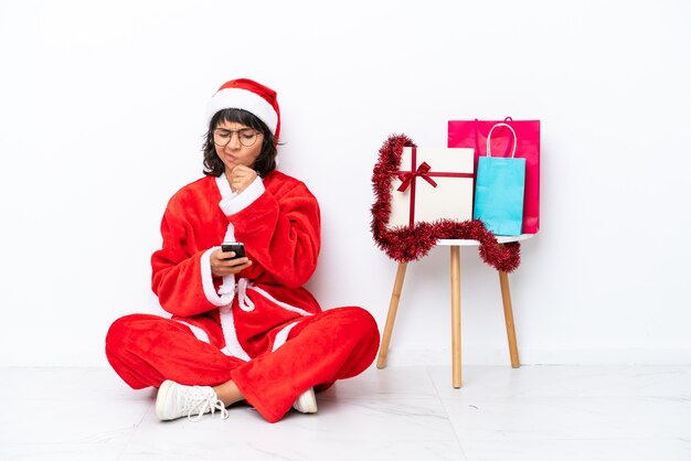 Jeune fille célébrant Noël assise sur le sol isolé sur fond blanc pensant et envoyant un message