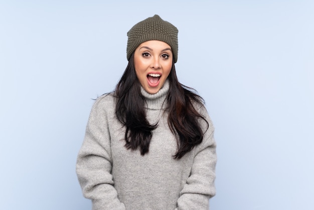 Jeune fille avec un chapeau d'hiver sur bleu avec une expression faciale surprise