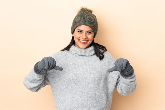 Jeune fille avec un chapeau d'hiver isolé sur beige fier et satisfait de lui-même