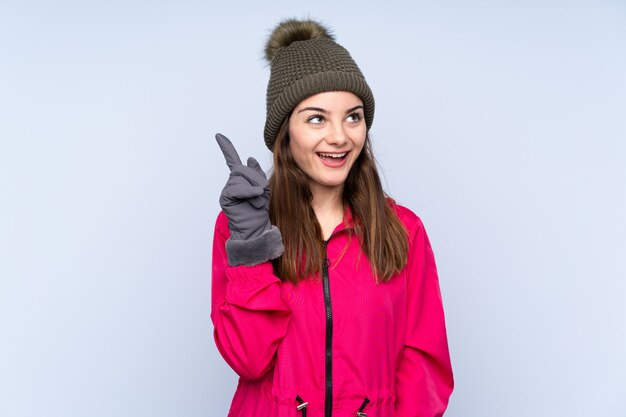 Jeune fille avec un chapeau d'hiver isolé sur bleu dans l'intention de réaliser la solution tout en levant un doigt