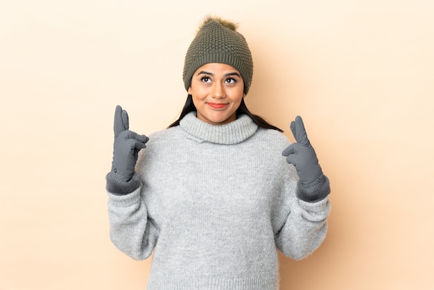 Jeune fille avec un chapeau d'hiver sur un mur beige avec les doigts croisés