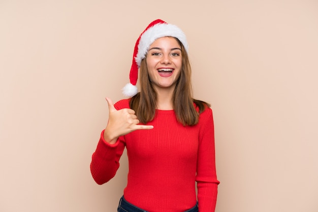 Jeune fille avec un chapeau de Noël sur mur isolé, geste de téléphone