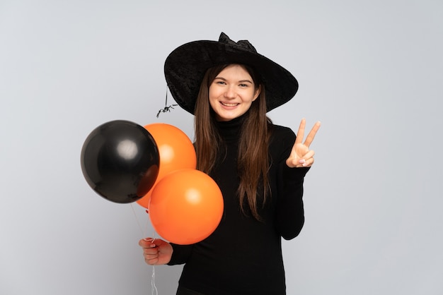 Jeune fille avec chapeau noir et robe noire tenant des ballons