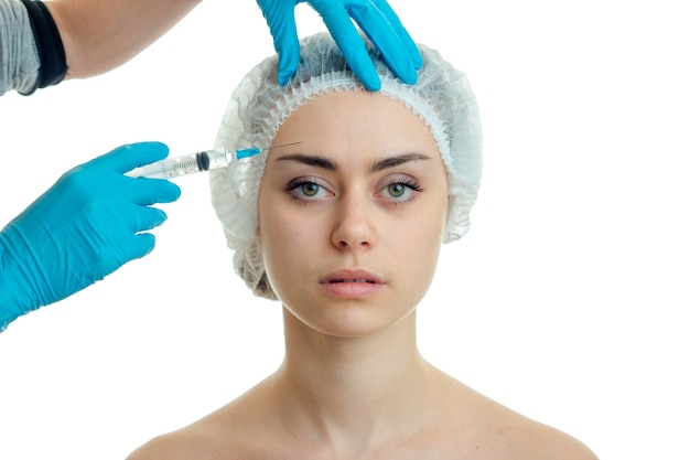 Une jeune fille avec un chapeau sur la tête et elle regarde directement faire des injections de remplissage facial isolées sur un gros plan de fond blanc