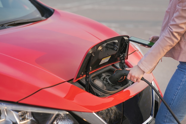 La jeune fille charge la voiture électrique à la gare. Femme branche un véhicule électrique pour charger la batterie de la voiture. Charge de voiture électrique dans la rue.