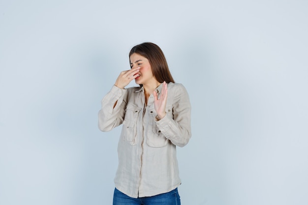 Jeune fille en chemise beige, jeans pinçant le nez à cause d'une mauvaise odeur et ayant l'air harcelé, vue de face.