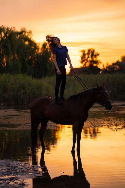 Une jeune fille sur un cheval sur un lac peu profond.