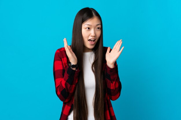 Jeune fille chinoise sur bleu isolé avec une expression faciale surprise