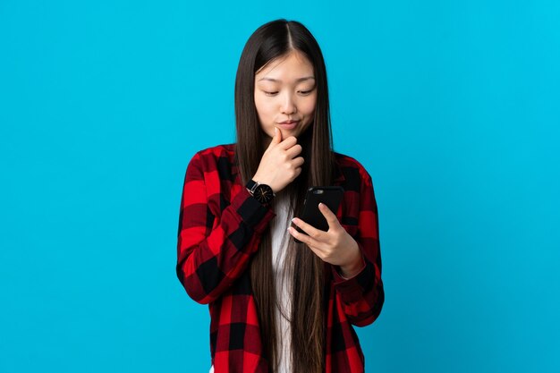 Jeune fille chinoise sur fond bleu isolé pensant et envoyant un message