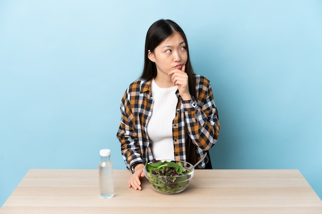Jeune fille chinoise mangeant une salade ayant des doutes et avec l'expression du visage confus