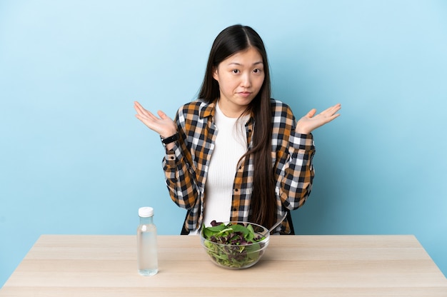 Jeune fille chinoise mangeant une salade ayant des doutes tout en levant les mains
