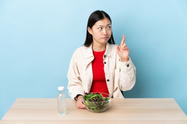 Jeune fille chinoise mangeant une salade avec les doigts croisés et souhaitant le meilleur