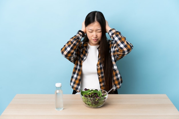 Jeune fille chinoise mangeant une salade frustrée et couvrant les oreilles