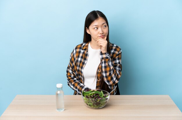 Jeune fille chinoise mangeant une salade en pensant à une idée tout en levant les yeux