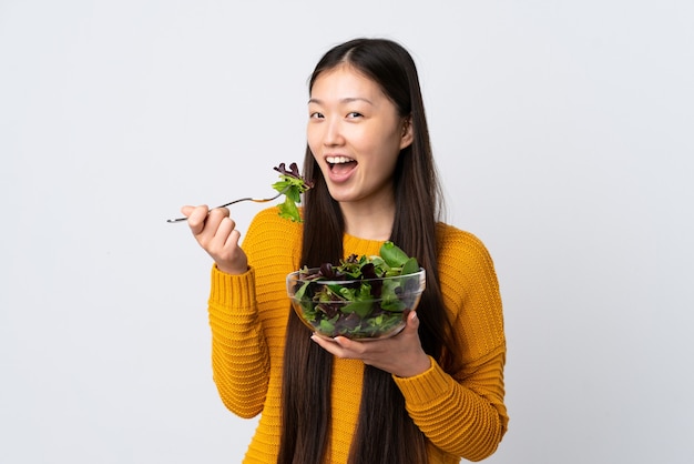 Jeune fille chinoise sur un mur blanc isolé tenant un bol de salade avec une expression heureuse