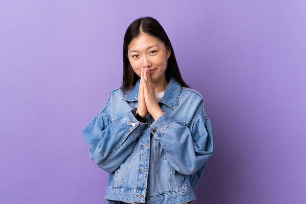 Jeune fille chinoise sur un mur violet isolé maintient la paume ensemble. La personne demande quelque chose