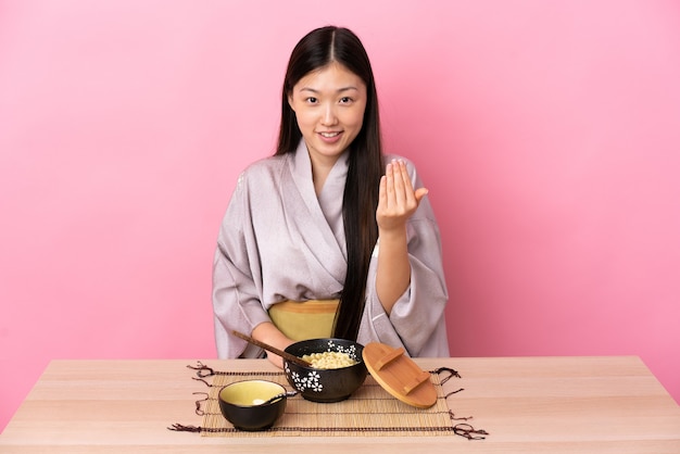 Jeune fille chinoise portant un kimono et mangeant des nouilles invitant à venir avec la main. Heureux que tu sois venu