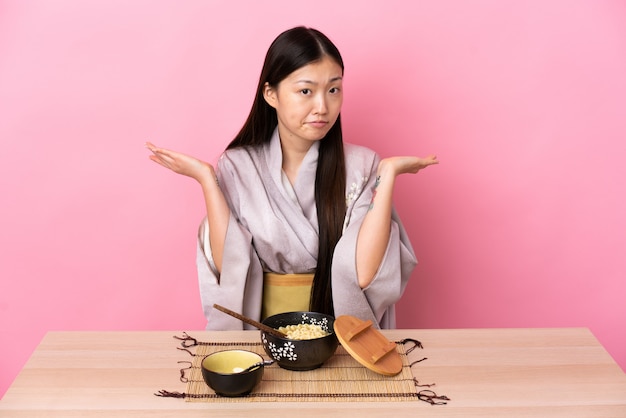 Jeune fille chinoise portant un kimono et manger des nouilles ayant des doutes tout en levant les mains