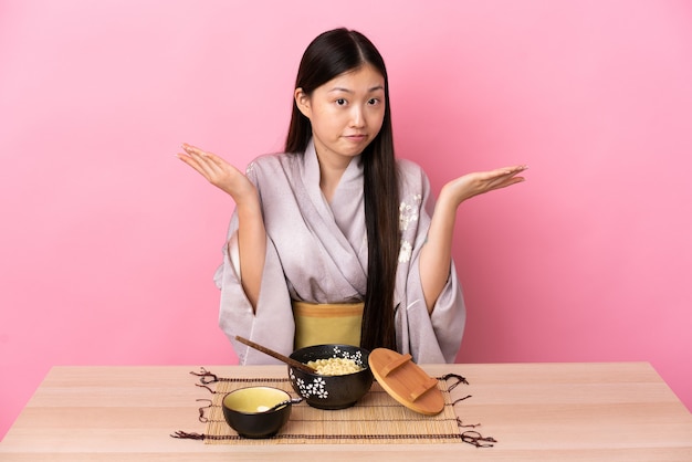 Jeune fille chinoise portant un kimono et manger des nouilles faisant le geste de doutes