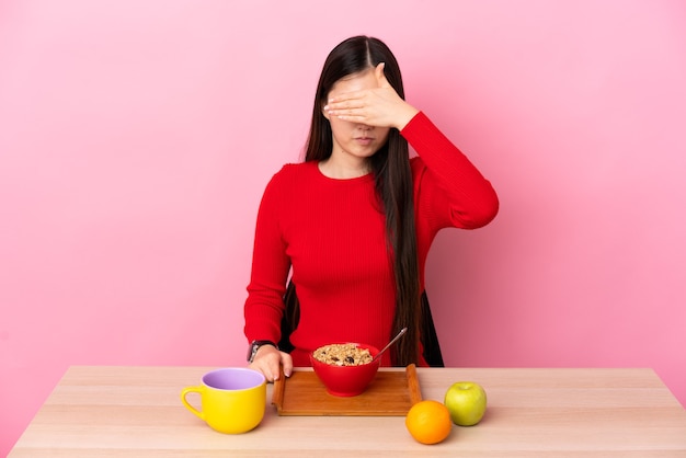 Jeune fille chinoise prenant son petit déjeuner dans une table couvrant les yeux par les mains. Je ne veux pas voir quelque chose