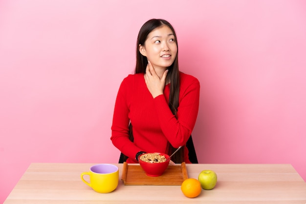 Jeune fille chinoise prenant son petit déjeuner dans une table à la recherche en souriant