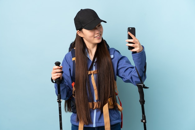 Jeune fille chinoise avec sac à dos et bâtons de randonnée sur le mur bleu faisant un selfie
