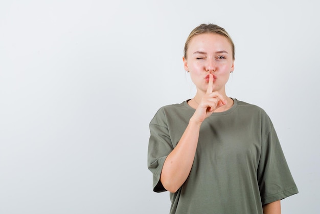 Jeune fille clignant des yeux et montrant un geste de silence sur fond blanc