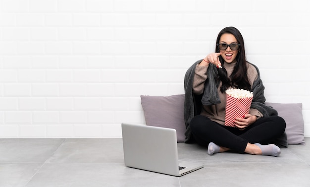 Jeune fille colombienne dans une pièce avec des lunettes 3d et tenant un grand seau de pop-corn tout en pointant devant