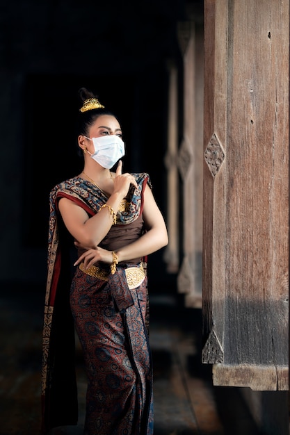 Photo la jeune fille en costume national thaïlandais portant un masque, dansant en position fermée. prévention des coronavirus