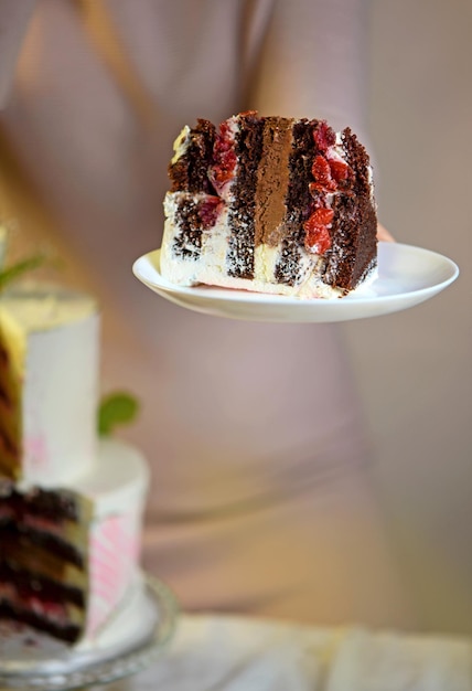 La jeune fille coupe et sert un morceau de gâteau gâteau de mariage festif à deux niveaux décoré de fleurs fraîches sur fond gris