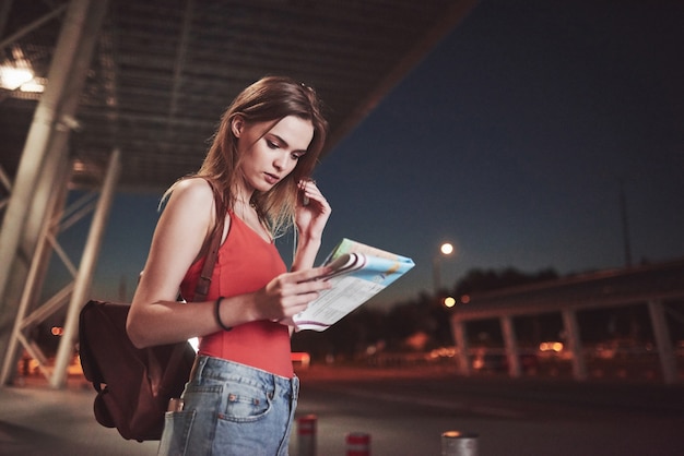 Jeune fille coûte la nuit près du terminal de l'aéroport ou de la gare et lecture du plan de la ville