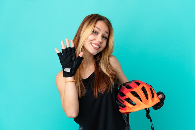 Jeune fille cycliste sur fond bleu isolé saluant avec la main avec une expression heureuse