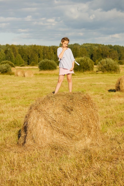 Jeune fille dans un champ d'été. sur un rouleau de foin.