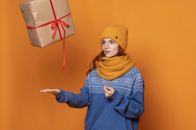 La jeune fille dans un chapeau et un chandail chauds tient un cadeau sur un fond jaune