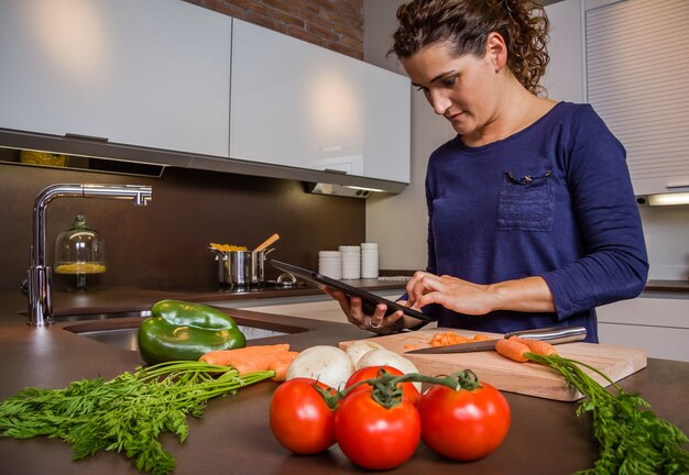 Jeune fille dans la cuisine à domicile préparant la nourriture et à la recherche de recette dans une tablette électronique. Concept de mode de vie moderne.