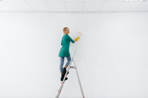 Une jeune fille dans les escaliers peint un mur blanc avec un rouleau