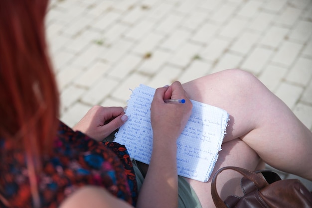 Photo jeune fille dans la nature écrivant sur une feuille de papier main et stylo créons quelque chose