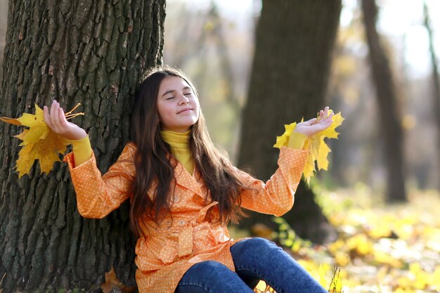 Jeune fille dans le parc au cours de l'automne avec des feuilles d'oranger sur les arbres