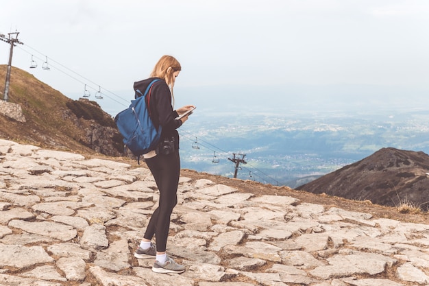 Jeune Fille Dans Un Pull Noir Et Des Jambières Se Dresse Dans Les Montagnes Et Utilise Le Téléphone