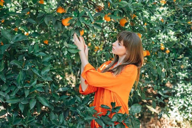 La jeune fille dans la robe orange tient l'orange dans l'arbre dans le jardin orange