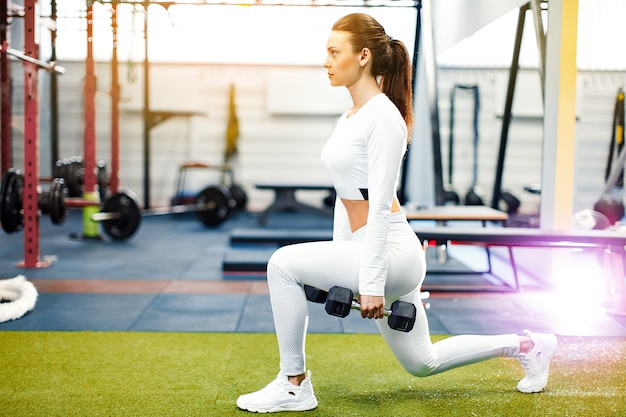 La jeune fille dans la salle de gym s'accroupit avec une barre.