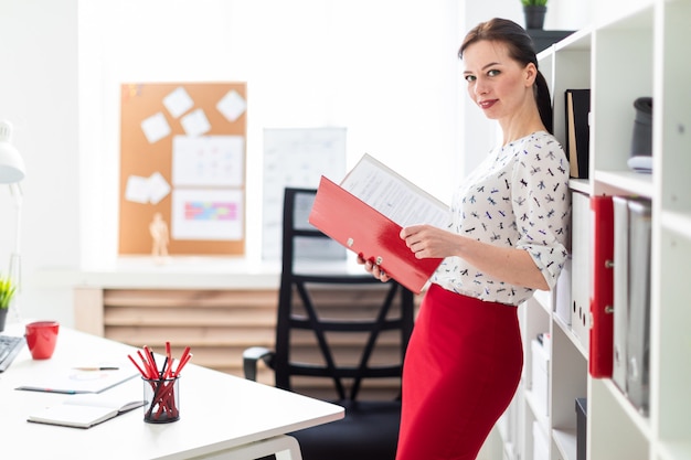 Une jeune fille debout dans le bureau et tenant un dossier rouge avec des documents