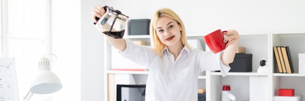 Une jeune fille debout dans le bureau et tenant une tasse et une cafetière.