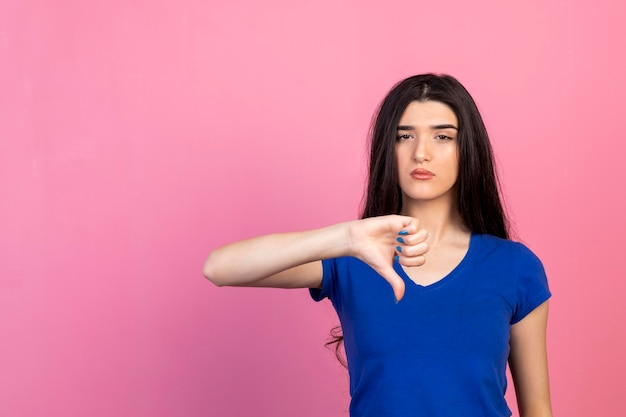 Jeune Fille Debout Sur Fond Rose Et Geste Pouce Vers Le Bas Photo De Haute Qualité