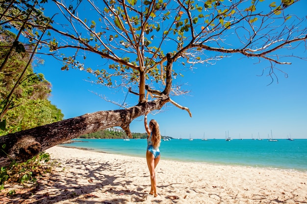 Jeune fille debout près de l'arbre sur la plage avec de l'eau claire