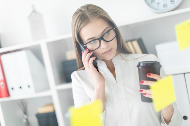 Une jeune fille debout près du Conseil avec des autocollants au bureau. Dans les mains de la jeune fille un verre de café et un téléphone