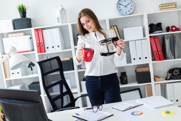 Une jeune fille debout près de la table et tenant une tasse et une cafetière.