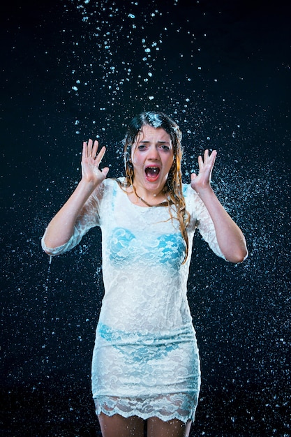 La jeune fille debout sous l'eau courante au fond de studio noir