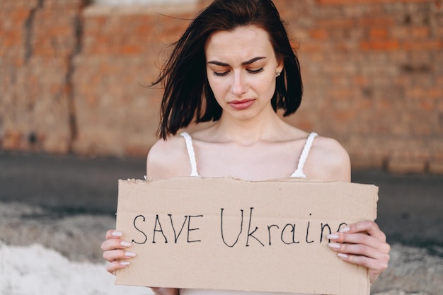 La jeune fille désespérée tient une pancarte dans ses mains et demande de sauver l'Ukraine pour arrêter la guerre